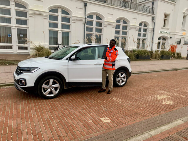 Notarzt Dr. Paul Okot-Opiro steht am Auto vor der Arztpraxis auf Juist
